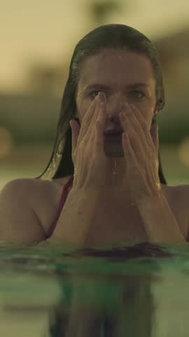 A young woman with wet hair and skin, wearing a red bikini top, is partially submerged in clear pool water