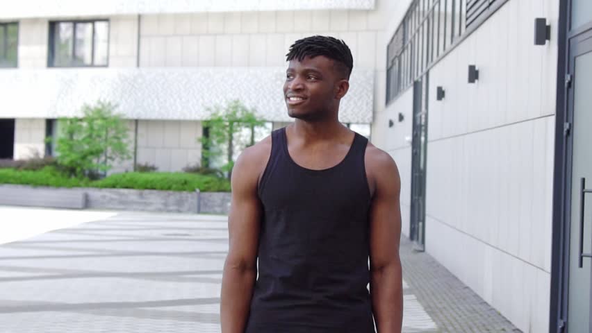 African American man in sportswear standing on city street and looking at camera, athletic guy crossing his arms and smiling
