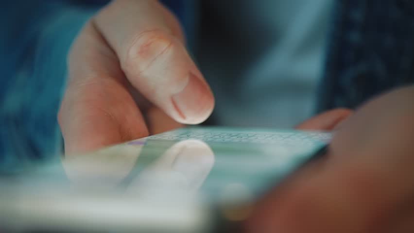 Close-up macro man in blue denim shirt typing on smartphone with one thumb while other hand holds device from below. Daylight indoor scene. Concept of mobile messaging and modern digital communication