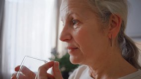 Senior woman takes painkiller with water sip in kitchen closeup. Elderly grey-haired lady uses medicine to reduce illness symptoms at home. Daily supplement - Powered by Shutterstock - Get 15% off with code: PIKWIZARD15