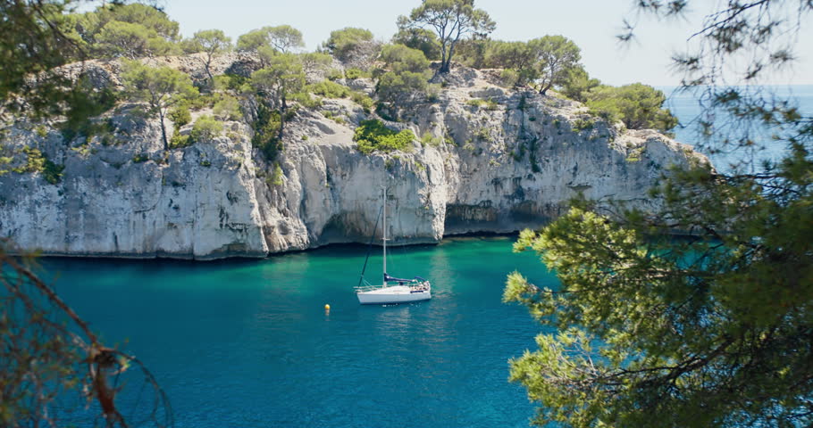 Sailing boat entering a narrow calanque near Cassis, France. Clear blue water, rocky cliffs and protected Mediterranean coastline