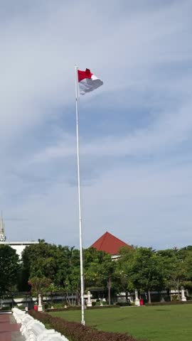 Surabaya, Indonesia - June 15, 2024, Indonesian flag fluttering on a high pole at Heroes Monument, Surabaya. Patriotic landmark under blue sky.