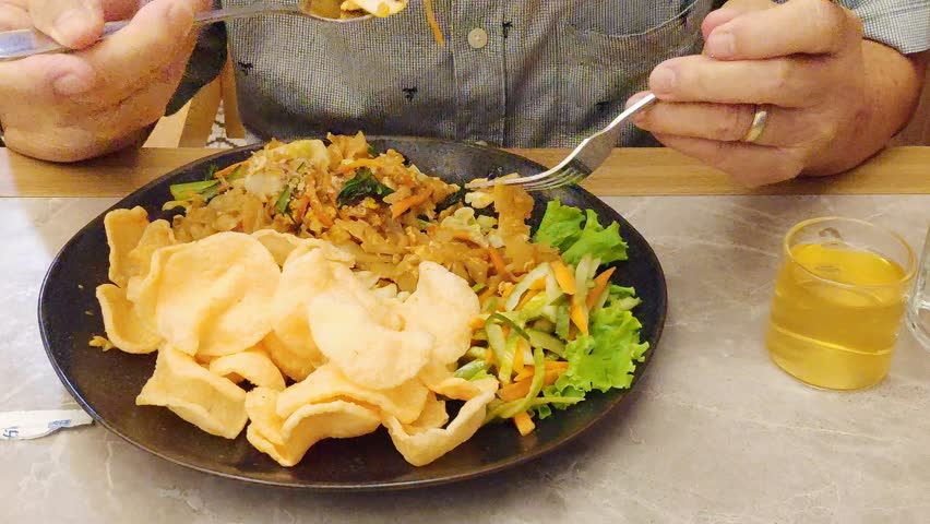Close up of an Asian man hands stirring fried rice noodles or Kwetiau Goreng with chicken on a plate.