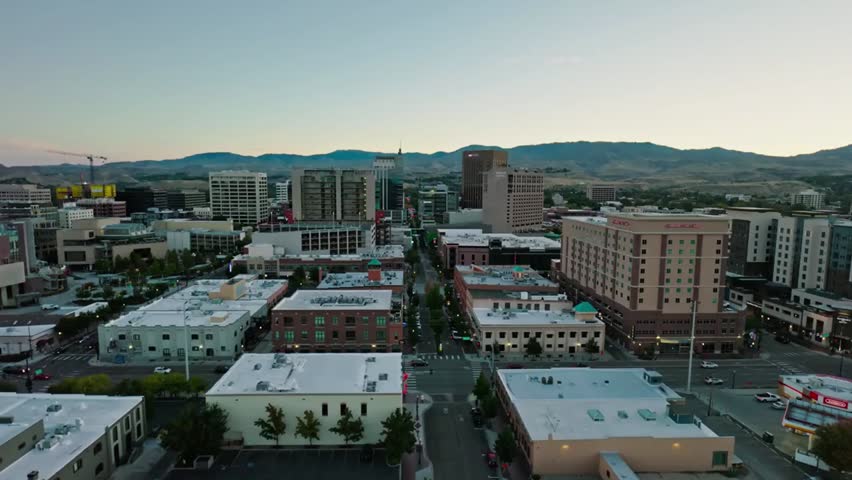 Aerial view of Boise, Idaho cityscape at dawn with mountains in the background, capturing urban and natural beauty in soft morning light.