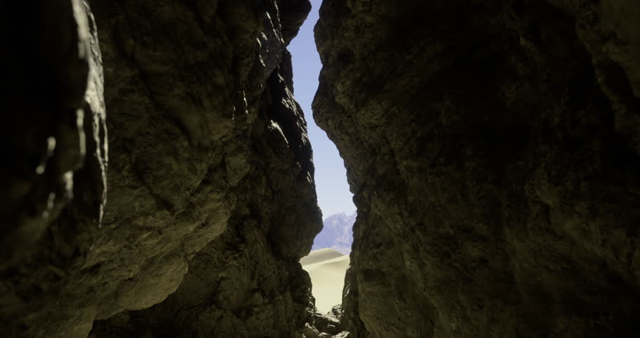 A rocky crevice frames a stunning view of a desert landscape under a clear blue sky. The sunlight illuminates the surrounding rock formations and distant sand dunes.