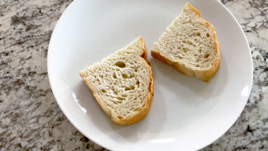 Slow motion- An egg salad sandwich is served open-faced on a white plate, accompanied by a slice of bread. The creamy texture of the filling is visible, and the plate is set on a kitchen counter. The