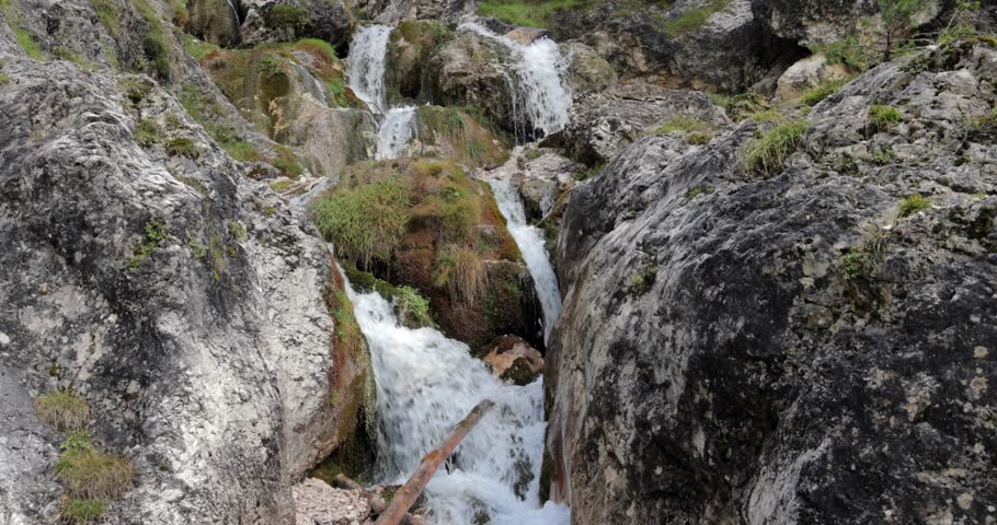 Alpine mountain stream in the Italian Alps cascades between huge boulders, clear cold water threads through mossy rocks and small ledges, bringing freshness and steady flow