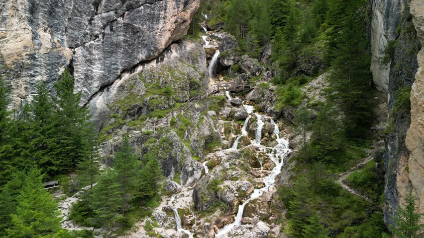 Hovering drone over Ciastlins waterfall gorge in South Tyrol Italy, tourists cross a wooden bridge while foaming streams race over boulders in a rock cleft