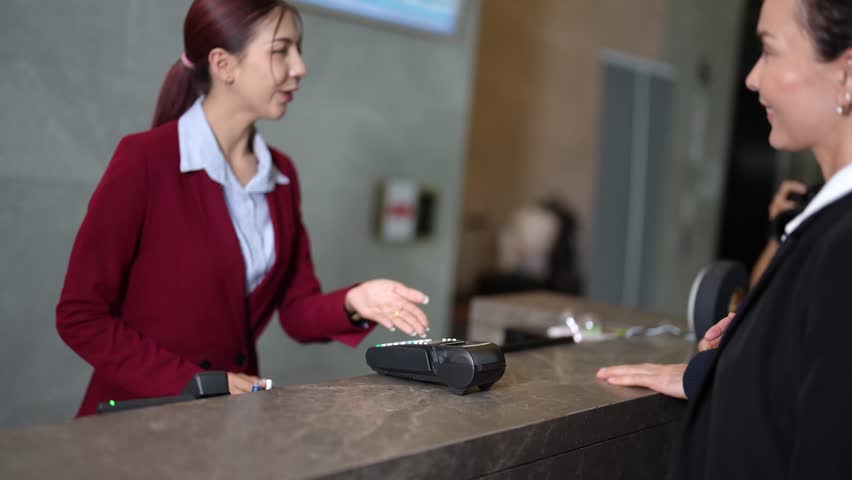 Traveling couple walking into hotel lobby and checking in at reception desk using credit card. Professional receptionist assists during smooth payment process before guests walk away. Hospitality and tourism concept.