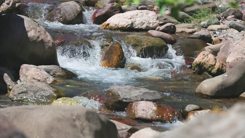 Close up of water rushing over stones creating small rapids and white foam in a mountain creek