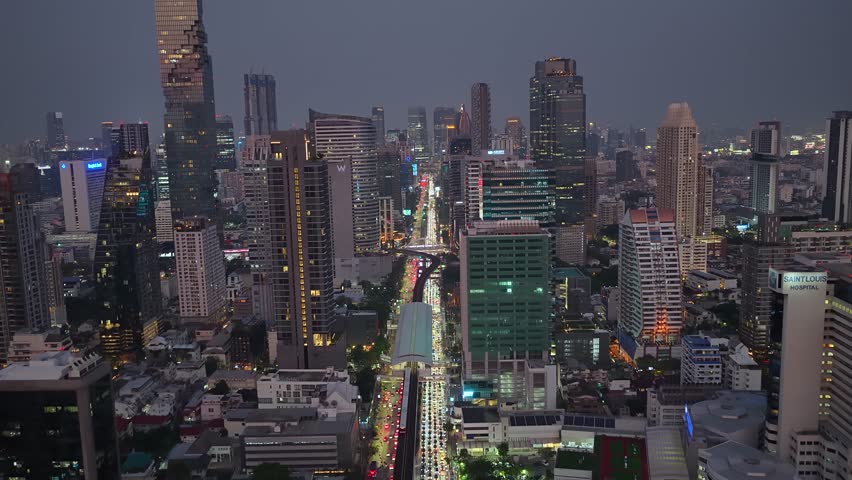 Real-time Aerial Night View Of Traffic Of Bangkok City With Towering Condos, Hotels And Corporate Offices In Thailand at Sunset or Sunrise. Flight Over the Wall Of Skyscrapers In Night Lights.