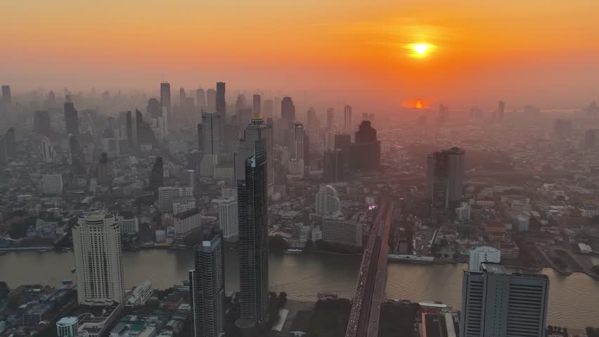 Real-time Aerial View Of Traffic Of Bangkok City With Towering Condos, Hotels, Corporate Offices and Traffic Jam In Thailand at Sunset or Sunrise. Flight Over the Wall Of Skyscrapers In Morning Light.