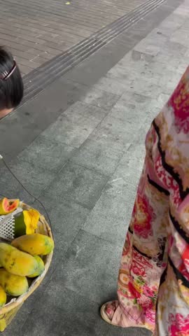 Street market scene in China with fresh mangoes for sale. Close view of mango trading, hands exchanging fruit, people negotiating price. Local street food market, Asian urban lifestyle, no visible faces.