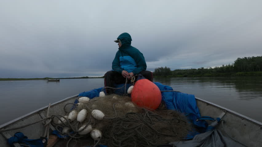 Lone fisherman wearing a rain jacket travels by boat with fishing gear on a cloudy day in alaska
