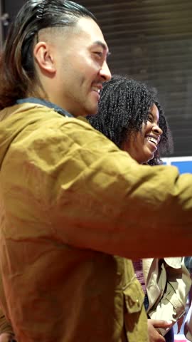 Young multiracial group of smiling friends standing in line and interacting while an asian man uses a modern touch screen terminal to sign up for a go kart competition at an indoor track