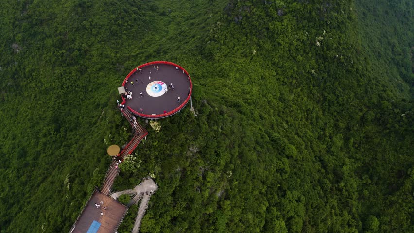 Descending view shows red circular platform atop lush karst cliffs in Yangshuo Gulin. Green slopes surround the structure blending nature and design for scenic travel footage.