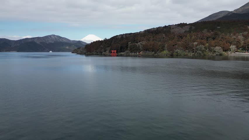 Peaceful view of Lake Ashi with calm water surface and mountain forest in background. Tranquil natural landscape in Hakone region. Overcast sky creating moody atmosphere at Japanese volcanic lake.