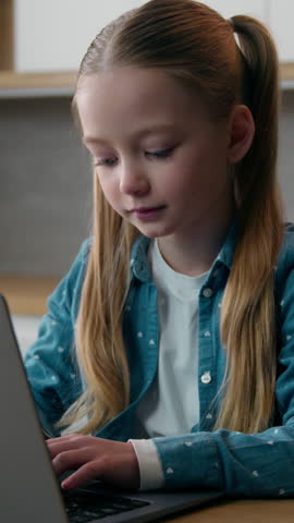 Caucasian girl child kid schoolgirl daughter at home kitchen using laptop online browsing family computer playing video game modern generation study internet lesson learning distant gadget addict