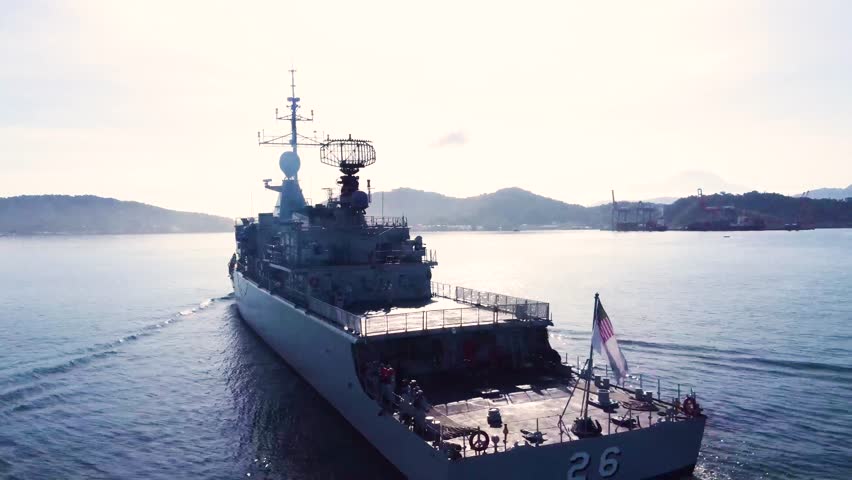 Naval destroyer sails at sunset leaving calm wake across tranquil coastal waters horizon.
