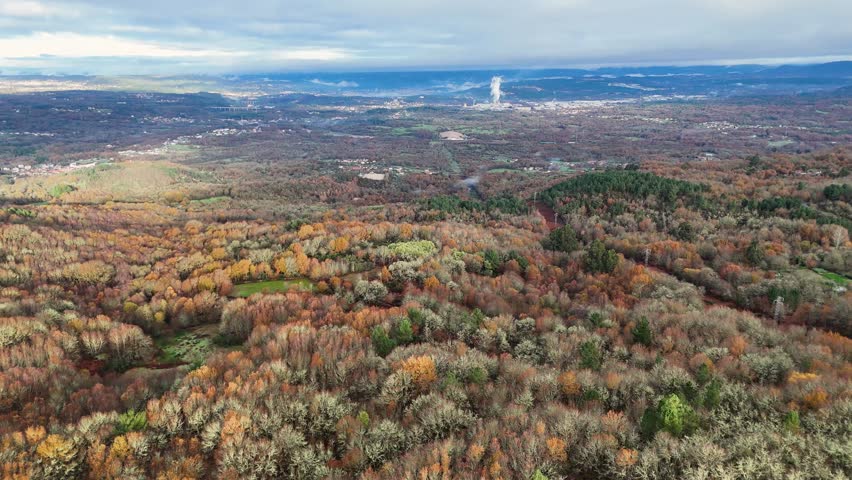 Drone flying over a beautiful autumn day with a view of a city and a forest. The sky is cloudy and the trees are covered in leaves in Orense, Spain.