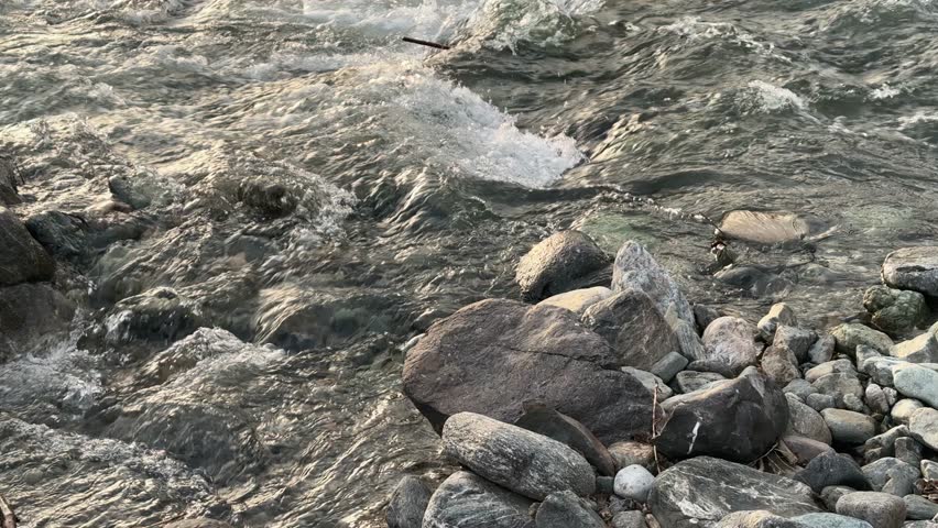 Close-up of mountain stream flowing over rocks, gradually merging into calmer larger river. Sunset light, trees and forest around. Beautiful nature scene.