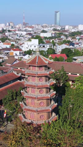 Aerial drone view of traditional pagoda tower in Hue, Vietnam. Historic Buddhist architecture rising above city skyline and residential rooftops in central Vietnam.