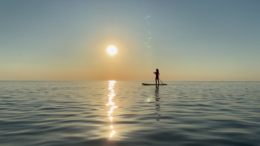 Young woman walking on stand up paddle sup boards by the sea during summer vacation. Beautiful woman flat water paddling against sea and sky background. Slow motion