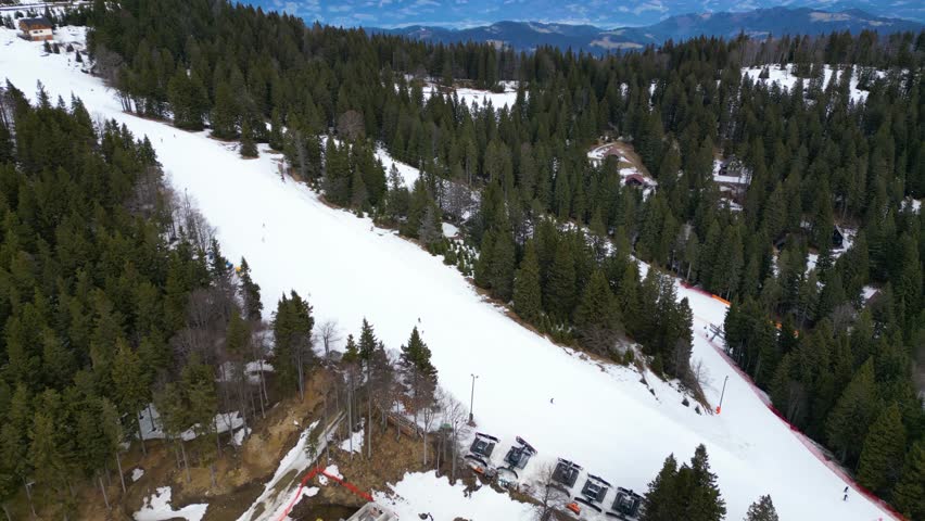 Aerial view of ski slope and chairlift at Kope ski center, Slovenia, with skiers on groomed piste, surrounded by forest and scenic winter mountains.