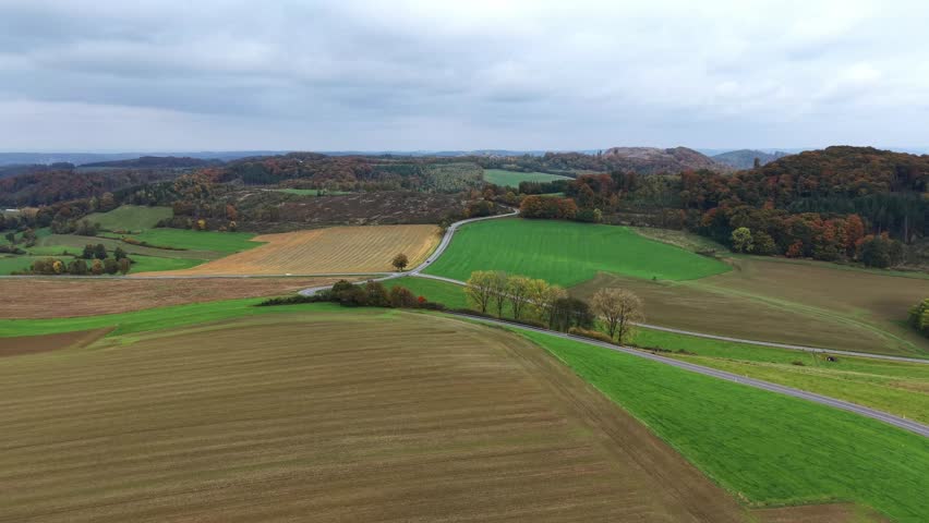Rural idyll from the air: A winding country road leads through a hilly landscape of fields.