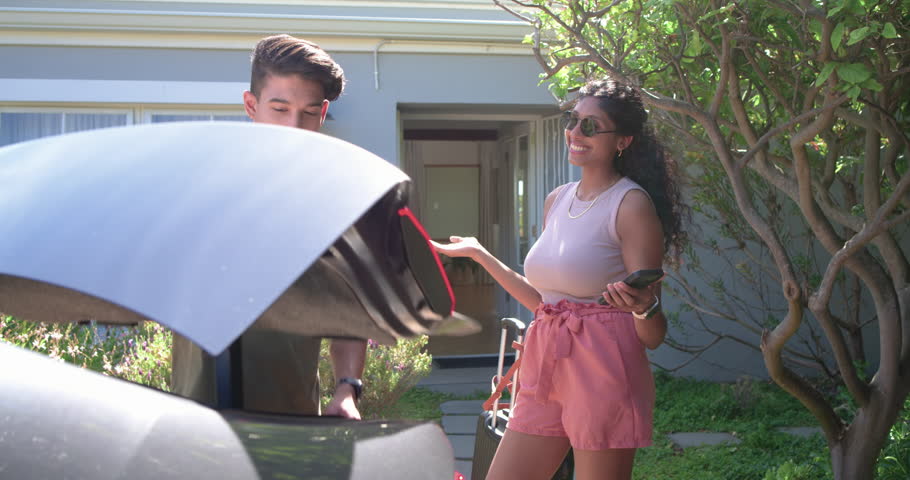 Couple loading suitcase after trunk opening, bringing luggage indoors, woman holding smartphone. Luggage, car, driveway, pair, casual, relaxed, frontyard