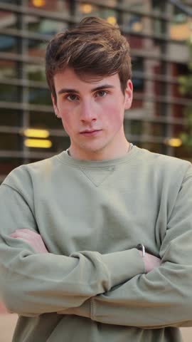 A focused young man gazes intently at the camera, showcasing a serious demeanor while crossing his arms, embodying confidence and determination in a purposeful pose that captivates the viewer.