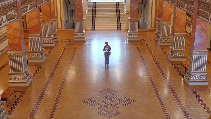 Businesswoman in an elegant suit runs into a luxurious hall, looks around, and leaves