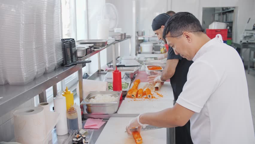 Sushi roll assembly in a busy commercial kitchen.