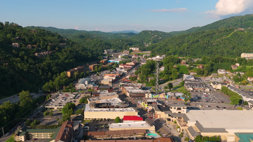 Aerial panorama of Gatlinburg, Tennessee with bustling main street filled with shops and attractions, observation tower and Smoky Mountains National Park nearby.