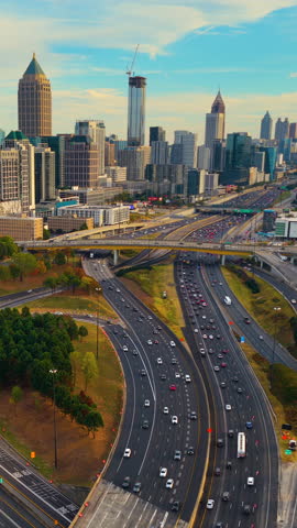 Complex freeway interchange cutting through Atlanta city landscape with tall skyscraper buildings, elevated roads, bridges and steady traffic. Dynamic urban environment.
