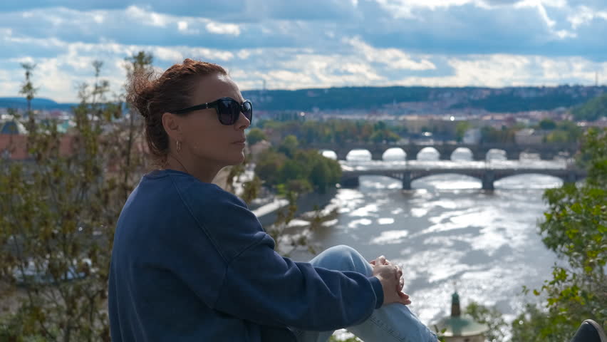 Tourist admiring prague cityscape and river. Woman tourist standing at scenic viewpoint overlooking sprawling prague landscape, capturing vltava river and historic bridges under bright sky