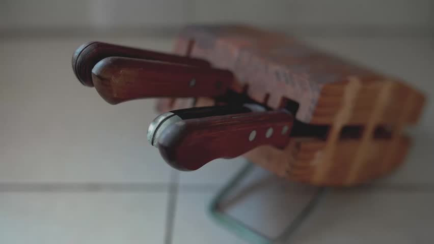Hand selecting sharp kitchen knife from wooden rack