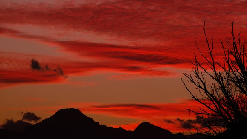 Cinematic Sunset Sky with Mountains and Bare Branches. Golden Hour Timelapse with Mountain and Tree Silhouette. Mountain Sunset with Bare Tree Branch Silhouettes. Fiery Sky at Dusk Behind Mountains and Dry Branches.