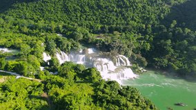 Spectacular aerial wide shot of the multi-tiered Ban Gioc Waterfall surrounded by lush green forests and limestone mountains under bright sunlight. - Powered by Shutterstock - Get 15% off with code: PIKWIZARD15