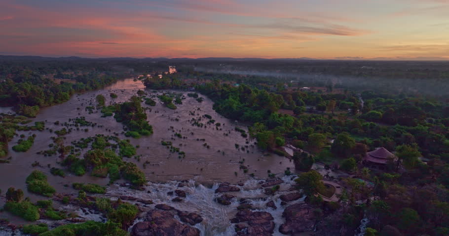 A dramatic aerial perspective captures turbulent currents rushing over layered stone barriers, forming one of Southeast Asia’s most iconic waterfall systems in the Si Phan Don region. Mekong River
