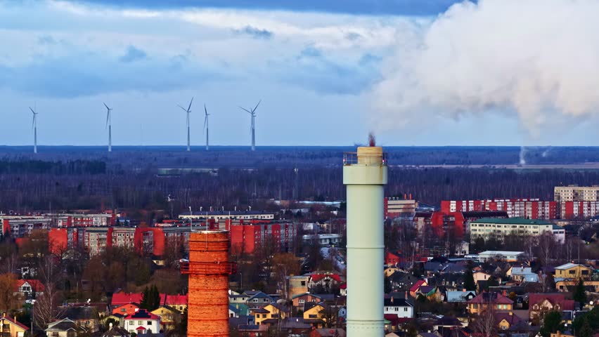 A panning view over houses and industry on the outskirts of Riga city, with a windmill field in the background.