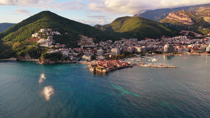 Aerial drone view of Budva, showing the Old Town surrounded by modern buildings and the lush mountains. Montenegro