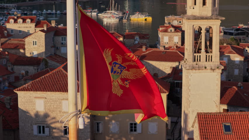 Aerial drone view of the Montenegro flag waving with Budva's Old Town and the marina in the background