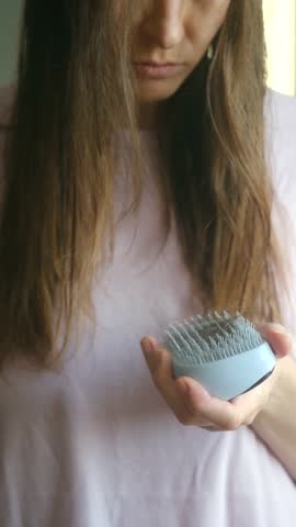 Unhappy young woman with long brown hair showing a clump of fallen hair from a scalp brush, demonstrating the concept of alopecia, shedding, hormonal imbalance, and hair health problems. Vertical