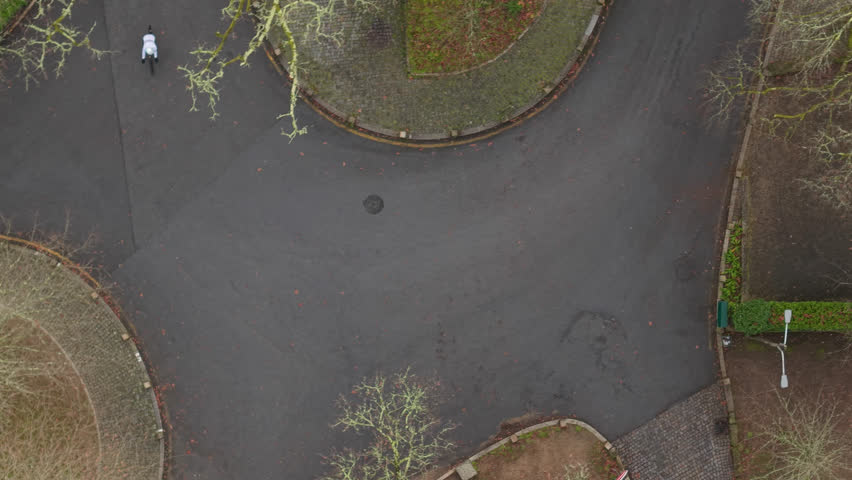 Drone view of cyclist crossing paved park junction on overcast day