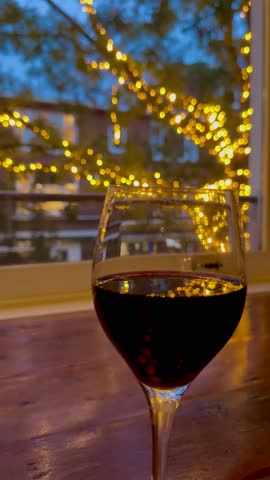 A cozy moment with a glass of red wine observing beautiful lights outside a window in the evening.