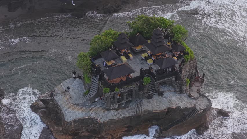 High angle view of the iconic tanah lot temple, a hindu shrine built on a rocky islet with waves crashing against its shores in bali