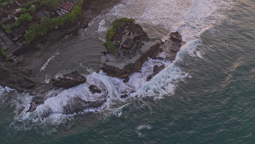Aerial view of the ancient tanah lot hindu temple on a rock formation in the sea with waves breaking against the shore during a beautiful sunset