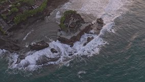 Aerial view of the ancient tanah lot hindu temple on a rock formation in the sea with waves breaking against the shore during a beautiful sunset - Powered by Shutterstock - Get 15% off with code: PIKWIZARD15