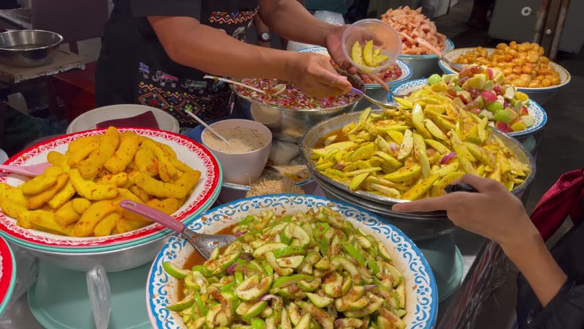 Colorful Thai street food stall preparing spicy fruit salads with mango, guava, and tropical fruits, mixed fresh by hand at a local market in Thailand